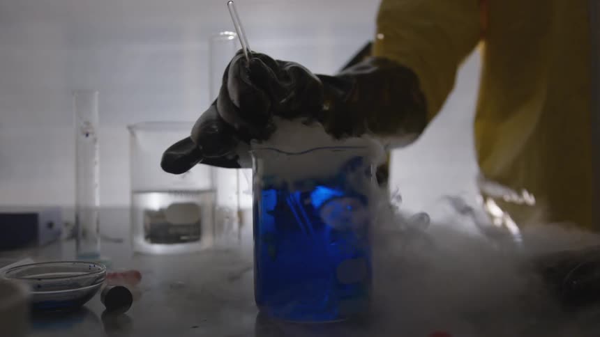 A person stirs a smoking blue liquid in a lab beaker