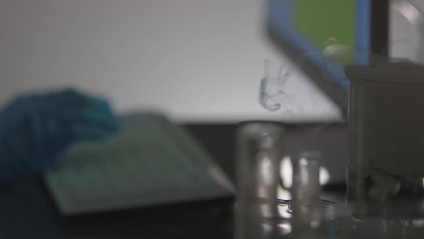 Someone types on a keyboard while a solution bubbles in a glass container