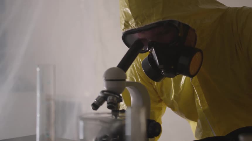A man in a hazmat suit looks through a microscope in a tented room