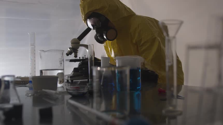 A man in a hazmat suit looks through a microscope