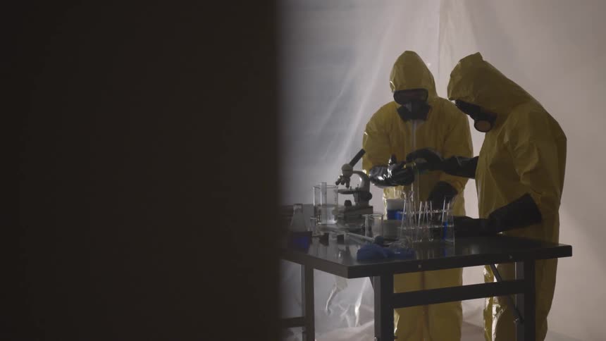 Two people in hazmat suits working with chemicals