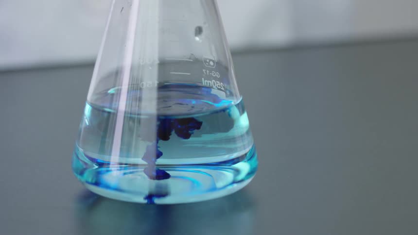 Droplets of blue liquid fall in to a solution in a beaker