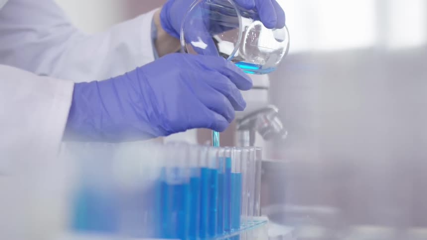 Technician pours from beaker into test tubes