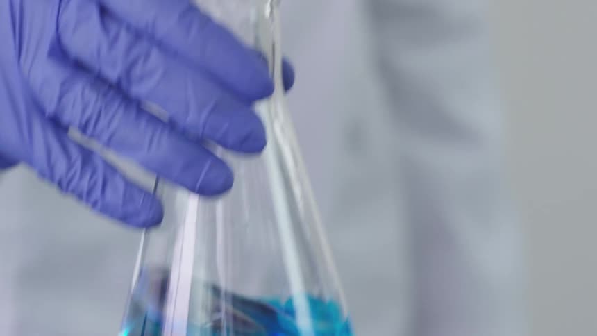 Chemist adding drops in a beaker then swirling the liquid