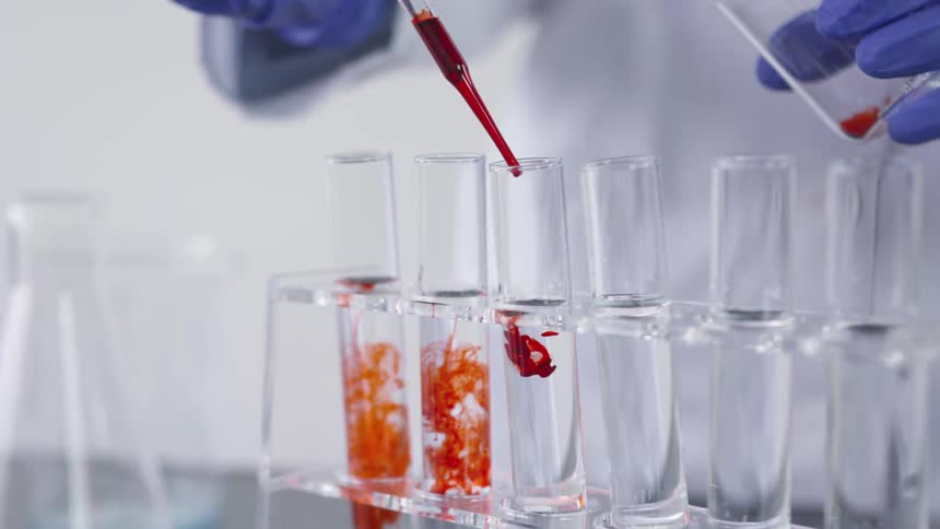 Technician drops red solution into test tubes