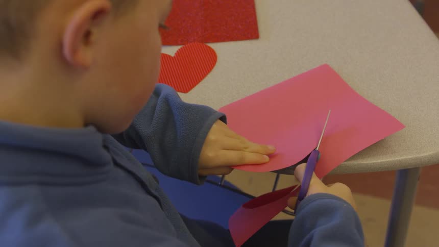 A young boy cuts red paper