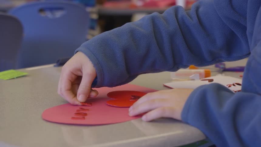 A child sitting at a table making heart artwork