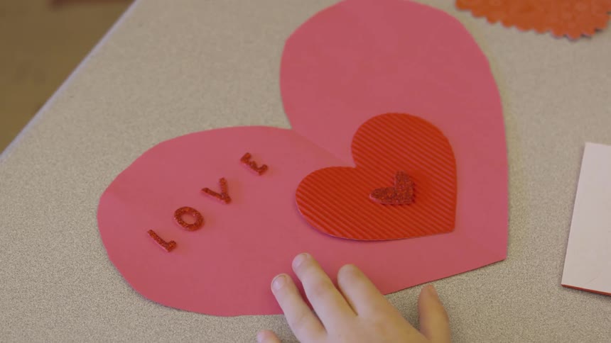Kid gluing letters on a cardboard heart