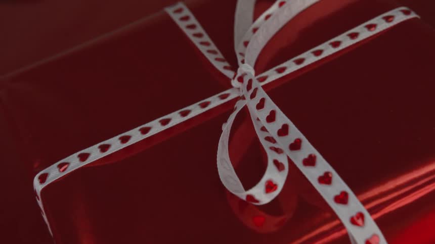 A gift for valentine's day is wrapped with red foil and has a bow with red hearts