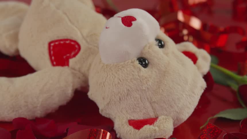 A teddy bear stuffed animal with hearts laying on a red background