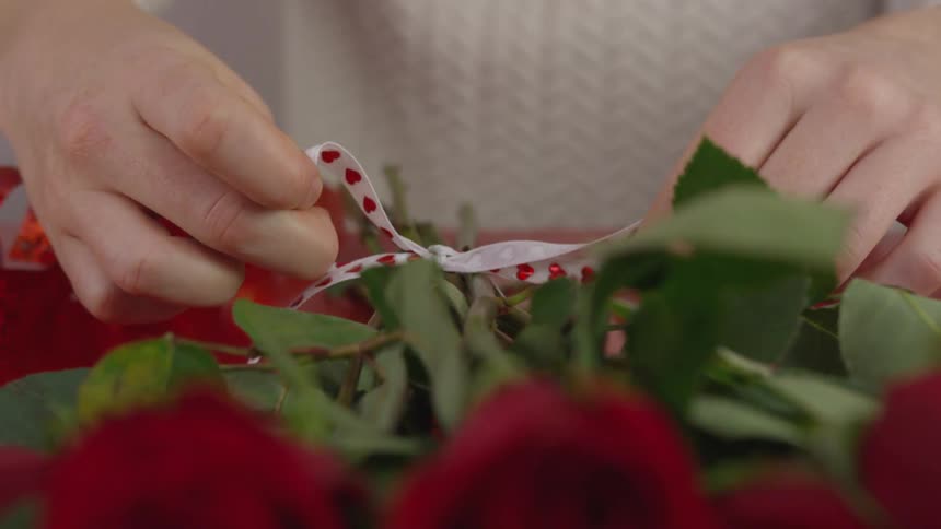 Person ties bow on stems of bunched roses