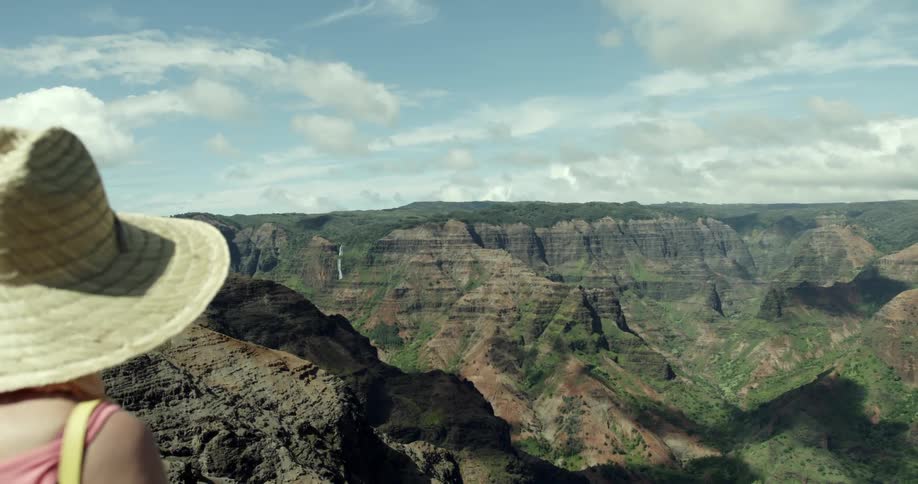 A woman stands and looks over a steep mountain range on a cloudy day