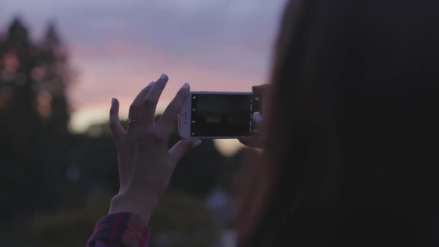 A woman photographing a sunset on her phone