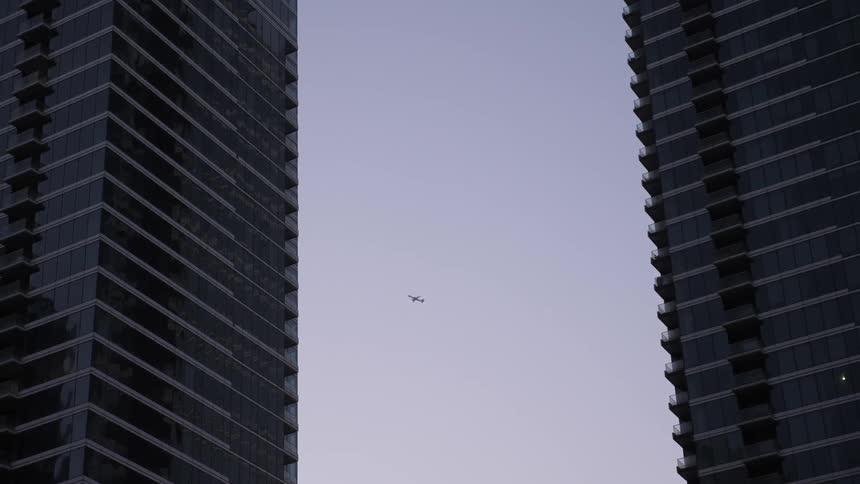 An airplane ascends toward the sky in between buildings