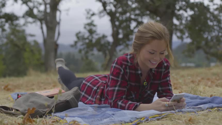 A young woman lay on a blanket on the ground while looking at her phone