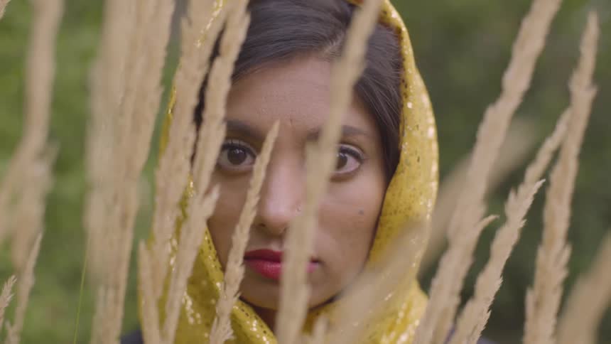 Woman in headscarf stands looking through tall stalks