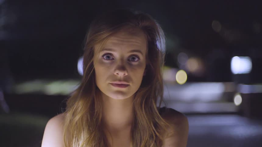 Young woman standing outside at night turns and looks at the camera