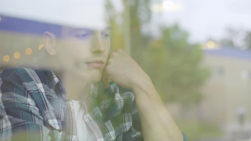 White male wearing a flannel sitting near a window looking nervous
