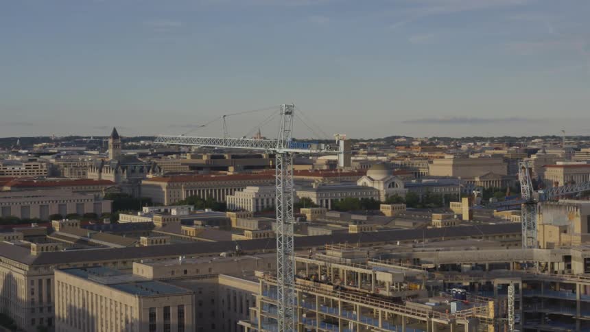 The camera circles around a crane in the middle of a city with hills in the distance