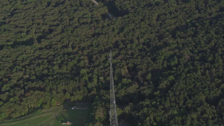 A large radio antenna with a field and forest in the background
