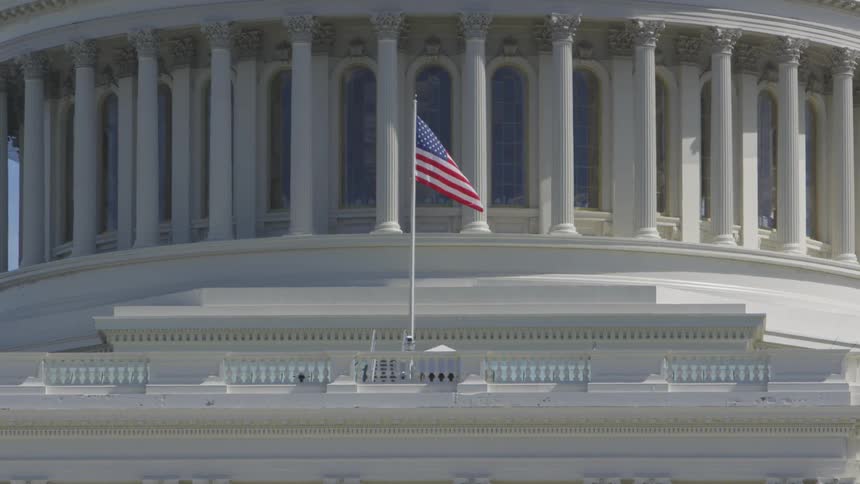A united states flag waving in the wind on top of the united states capitol building