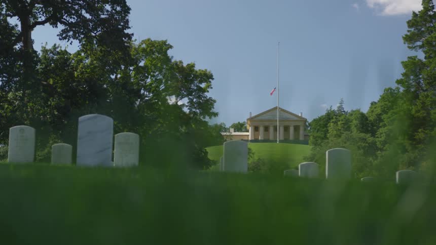 The flag is flying half mast as the headstones stand proudly on a bed of bright spring green the monument in the background