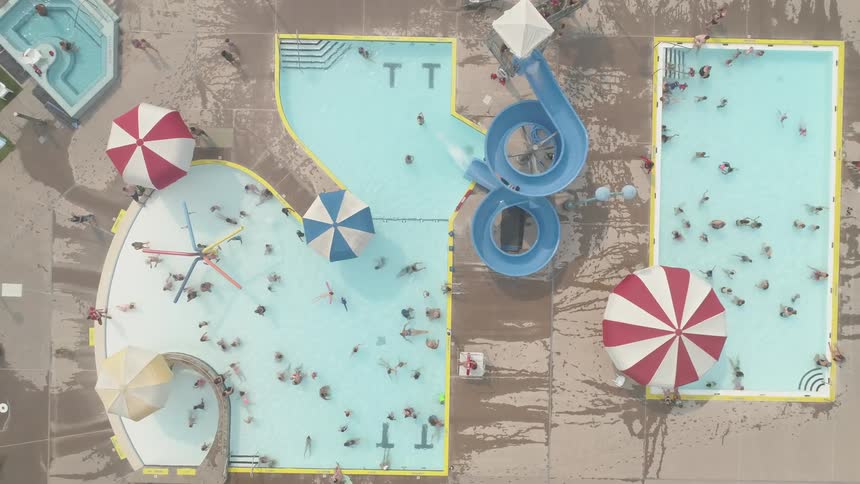 Three busy public pools lie far below as people go down a slide into the largest pool