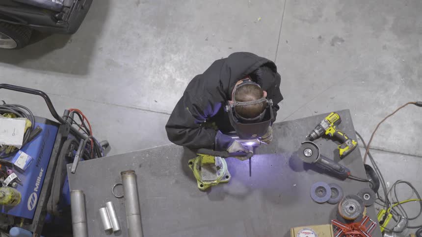 A man welding something at a bench in a garage