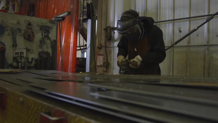 A metal worker uses a power grinder on sheets of metal causing sparks to fly