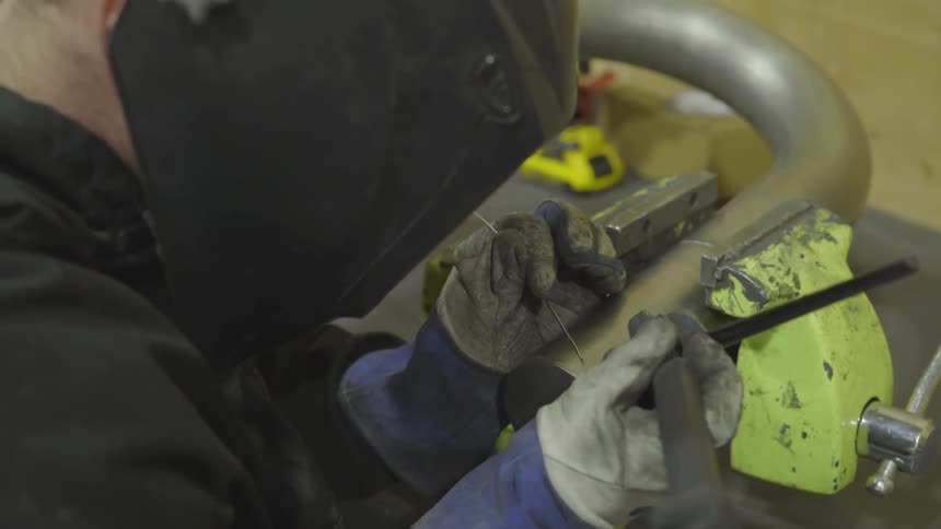 The welder is welding what appears to be the top lock portion of a giant padlock