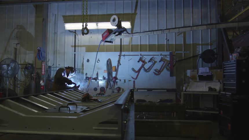 A person is welding a metal object inside a dark shop surrounded by tools
