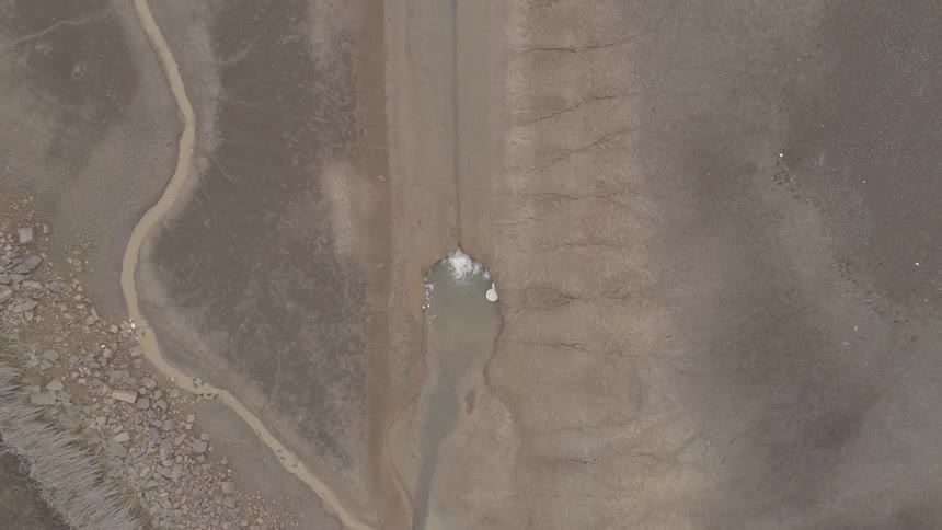 It is an aerial of a big muddy ugly looking rock with water squirting into it lifting up and looking at a road