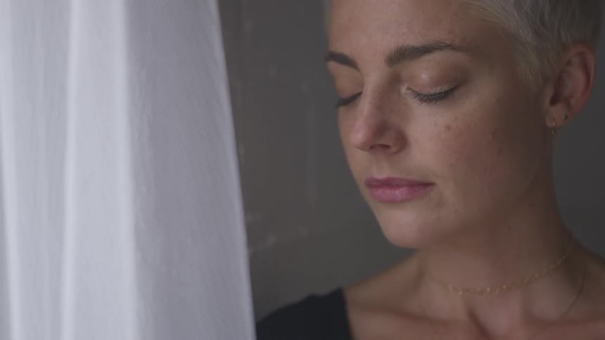 Short hair woman closes her eyes next to the white curtain in the daytime