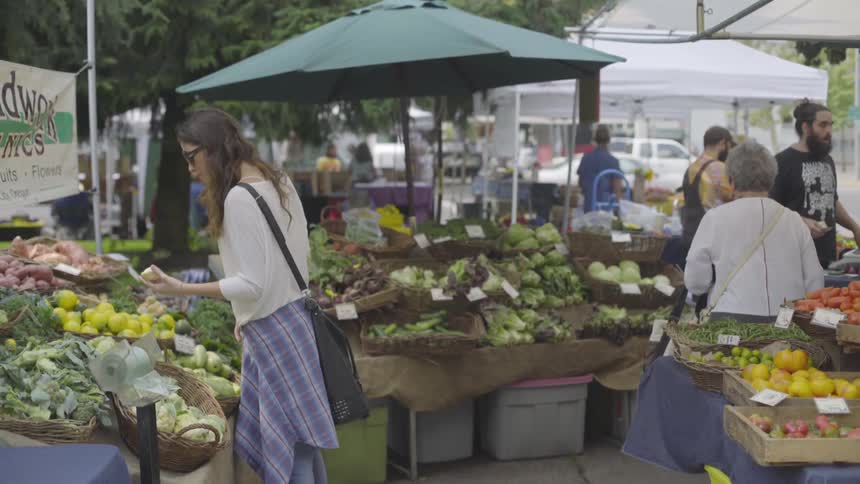 A young woman shops for vegetables at an outdoor farmers market
