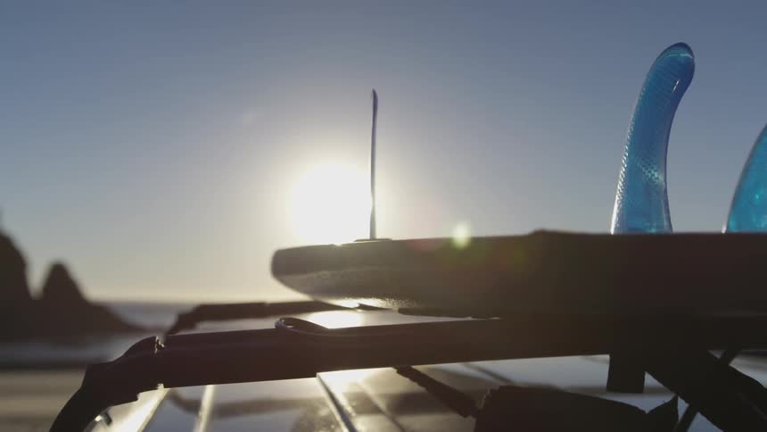 A surfboard mounted to the top of a vehicle on the beach