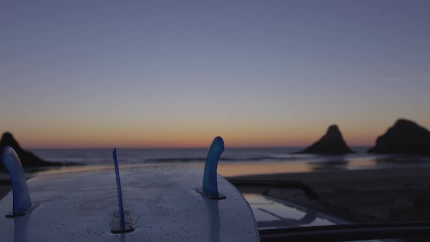 A surfboard on top of a vehicle parked at a beach shore