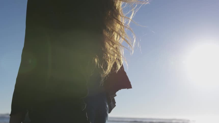 Back of person's torso with hair flowing down under a clear blue sky