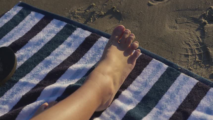 A person's feet on a towel on a beach