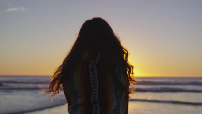 A woman stands along the shoreline looking to the horizon