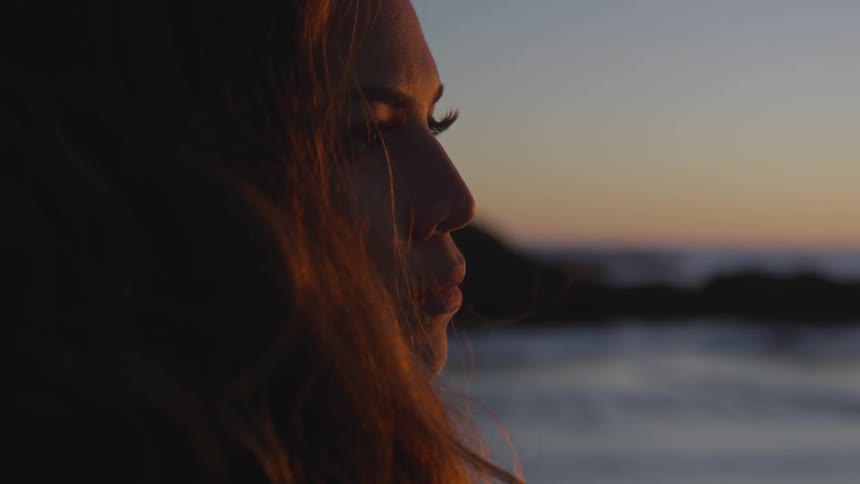 Woman stands on beach and look out to sea during sunset