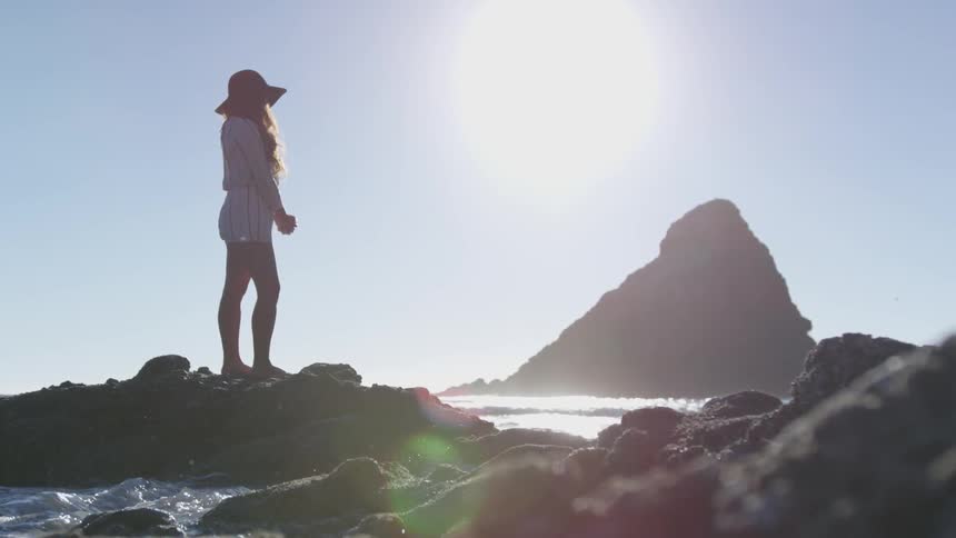 Woman standing on the rocks of a beach at morning