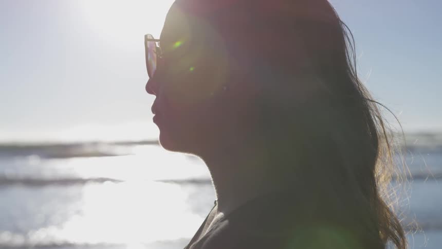 A woman wearing sunglasses looks out over the ocean