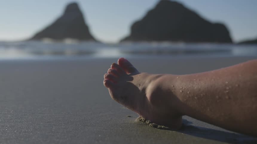 Water beads on a woman's leg as her foot rests in the wet sand on the beach