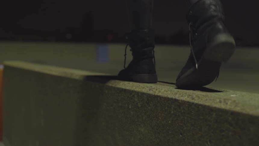Person balances across low wall on building rooftop at night