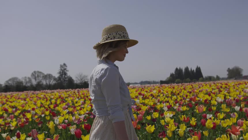 White woman wearing a hat walking across a flower field