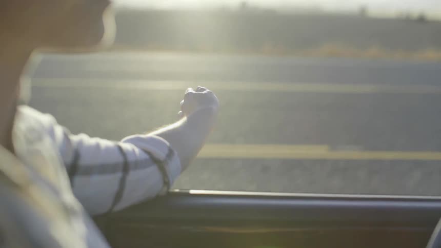 A woman is in a car with her arm hanging out the window