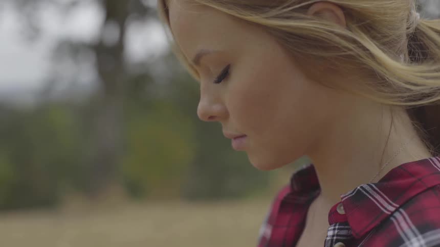 A blonde woman stands outside with her eyes closed as the wind blows her hair