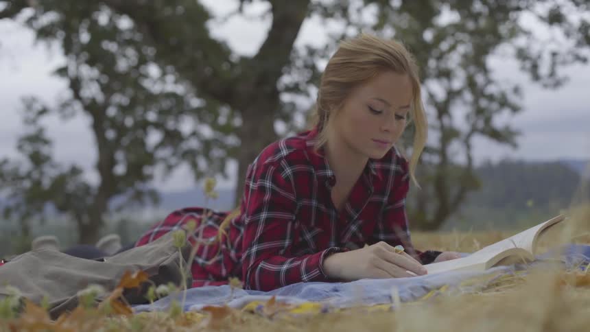 Young woman lies in field reading book