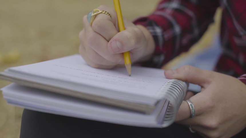A woman uses a pencil to write in a spiral notebook