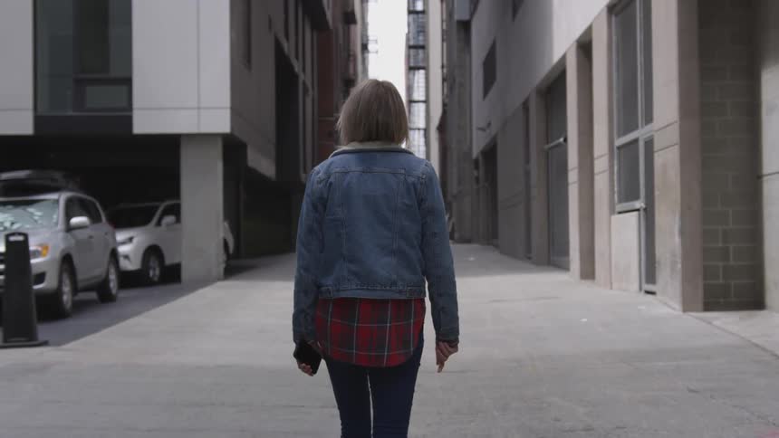 A woman walks down a sidewalk between buildings